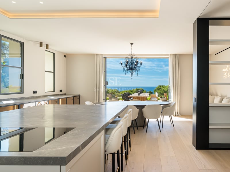 Cuisine haut de gamme avec îlot en marbre et salle à manger surplombant la Méditerranée par de grandes baies vitrées.