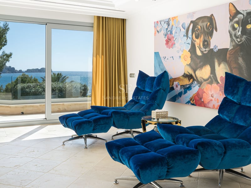 Deux fauteuils de salon en velours bleu avec repose-pieds dans une pièce lumineuse offrant une vue sur la mer.