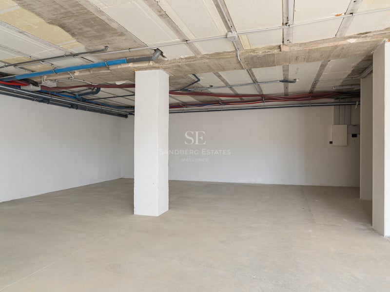 Grand parking souterrain en béton avec tuyauterie apparente et une colonne de soutien blanche.