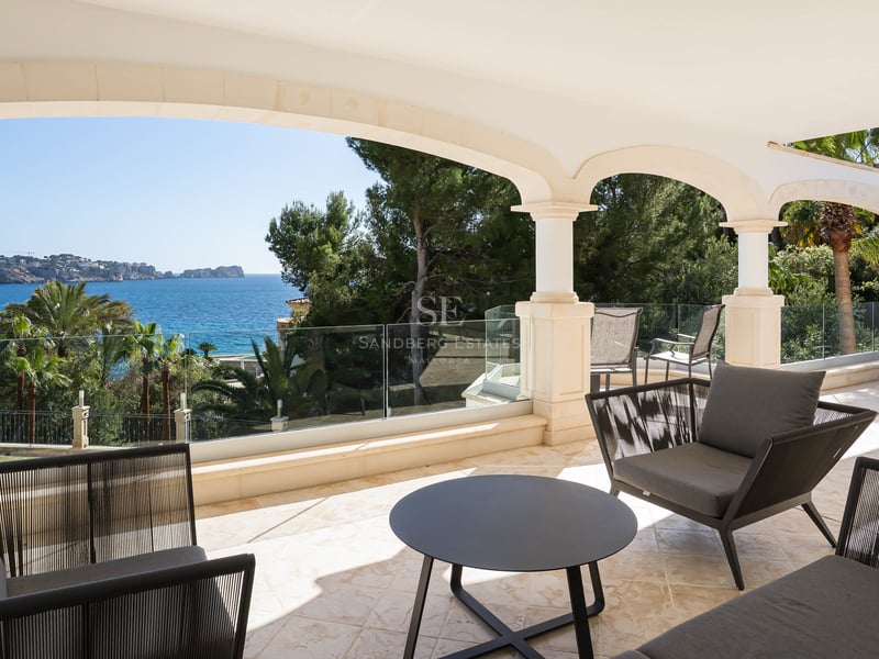 Terrasse couverte en pierre avec arches, garde-corps en verre et mobilier moderne surplombant la Méditerranée.