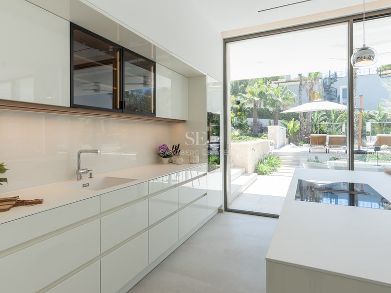 Cuisine blanche laquée moderne avec de grandes baies vitrées ouvrant sur un jardin méditerranéen.