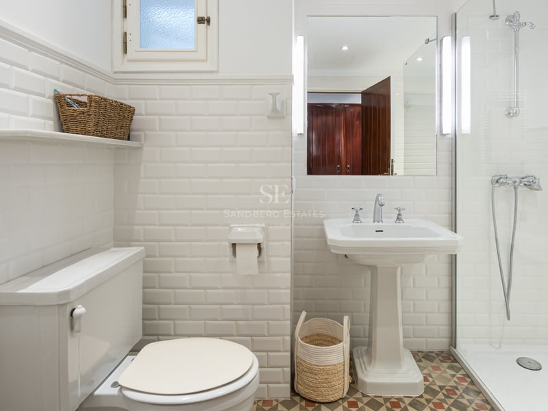 Salle de bain lumineuse avec carrelage métro blanc, lavabo sur colonne, douche vitrée et sol à motifs.