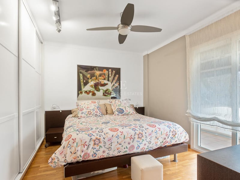 Chambre avec parquet en chêne, placards intégrés blancs, lit double et porte vitrée donnant sur terrasse.