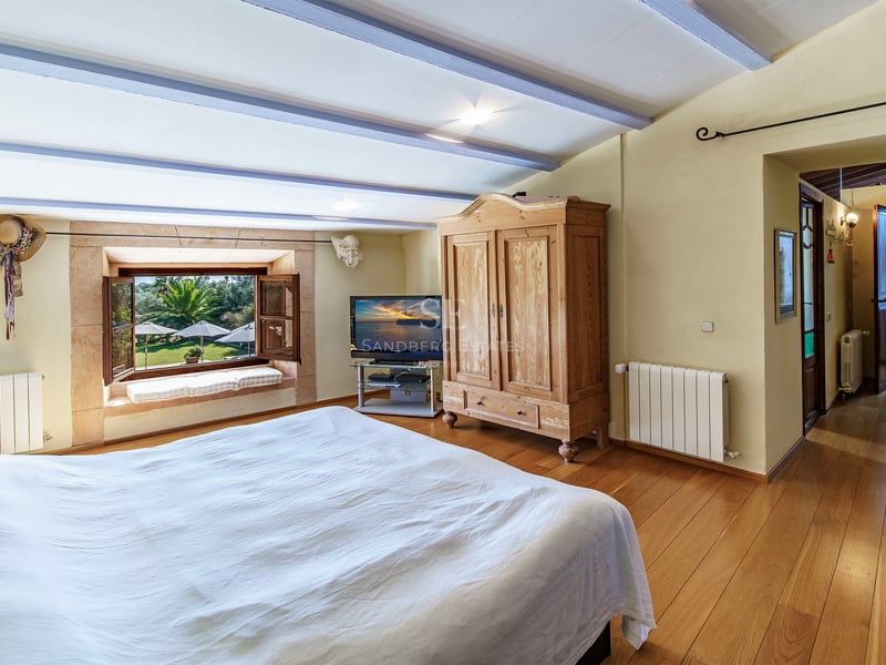 Chambre chaleureuse avec parquet en bois, armoire rustique et fenêtre donnant sur un jardin luxuriant.
