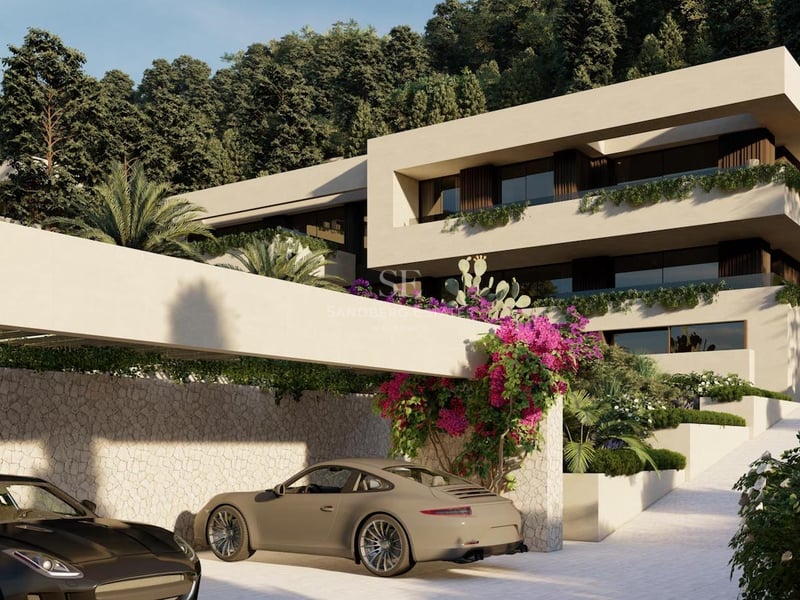 Façade de villa moderne blanche avec voitures de luxe, murs en pierre et bougainvilliers sur un flanc de colline.