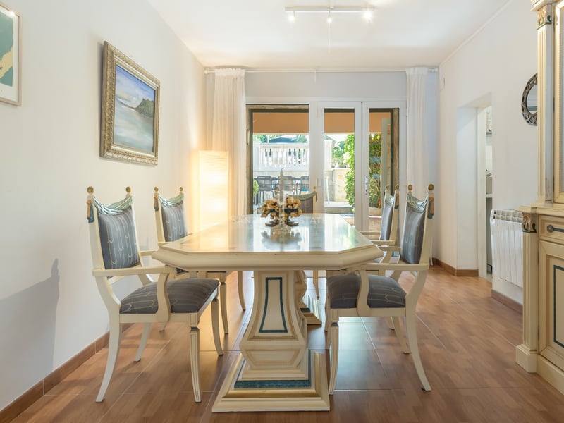 Salle à manger lumineuse avec table et chaises ornées crème et bleu, vitrine assortie et vue sur la terrasse.