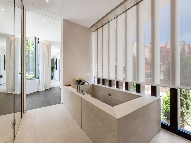 Salle de bain minimaliste avec baignoire rectangulaire en pierre, parois vitrées et grandes fenêtres.