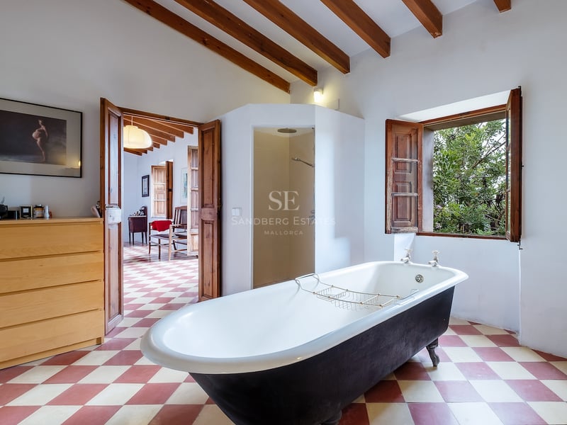 Salle de bain spacieuse avec baignoire îlot noire, poutres en bois apparentes, sol à damier et vue sur le jardin.
