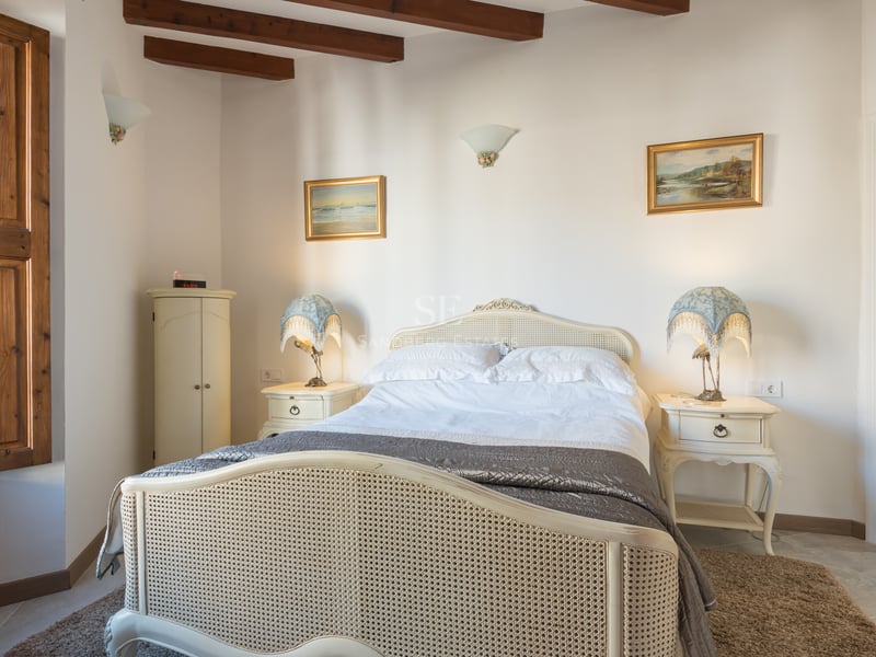 Chambre chaleureuse avec lit en rotin, poutres en bois au plafond et volets intérieurs traditionnels.