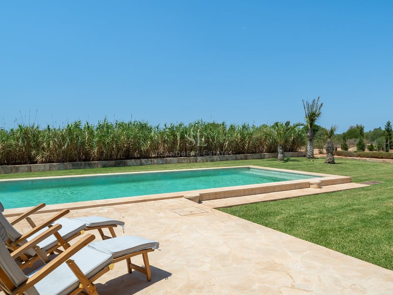 Piscina rectangular de agua turquesa con terraza de piedra natural, tumbonas de madera y césped cuidado.