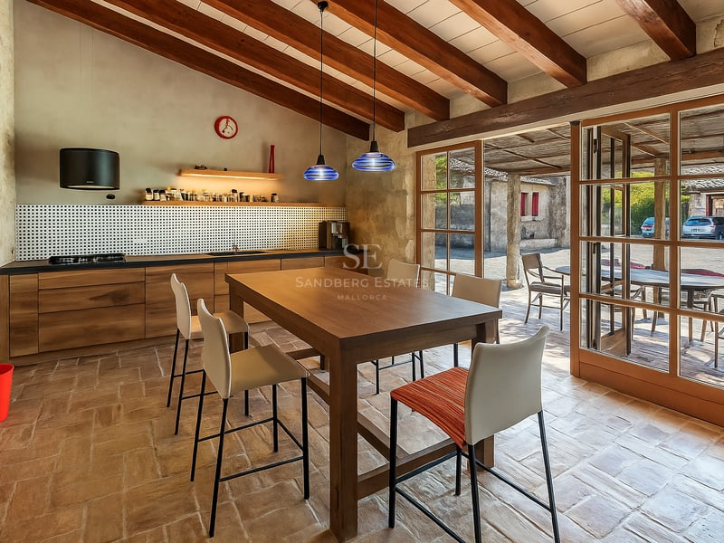 Cuisine avec poutres apparentes, sol en terre cuite et grandes portes vitrées ouvrant sur l'extérieur.