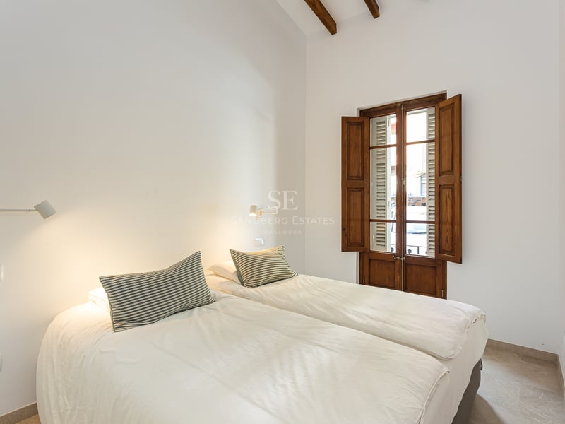 Chambre minimaliste blanche avec deux lits, hauts plafonds avec poutres et volets traditionnels en bois.