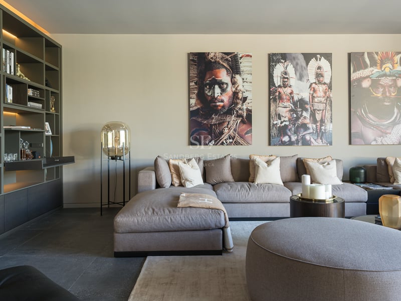 Salon moderne avec un grand canapé modulaire gris, une bibliothèque intégrée et trois portraits tribaux au mur.