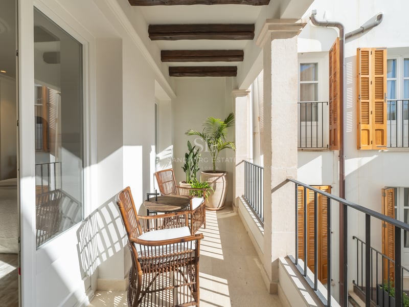 Sun-drenched private terrace with wicker seating, exposed wooden beams, stone pillars, and traditional wooden shutters.