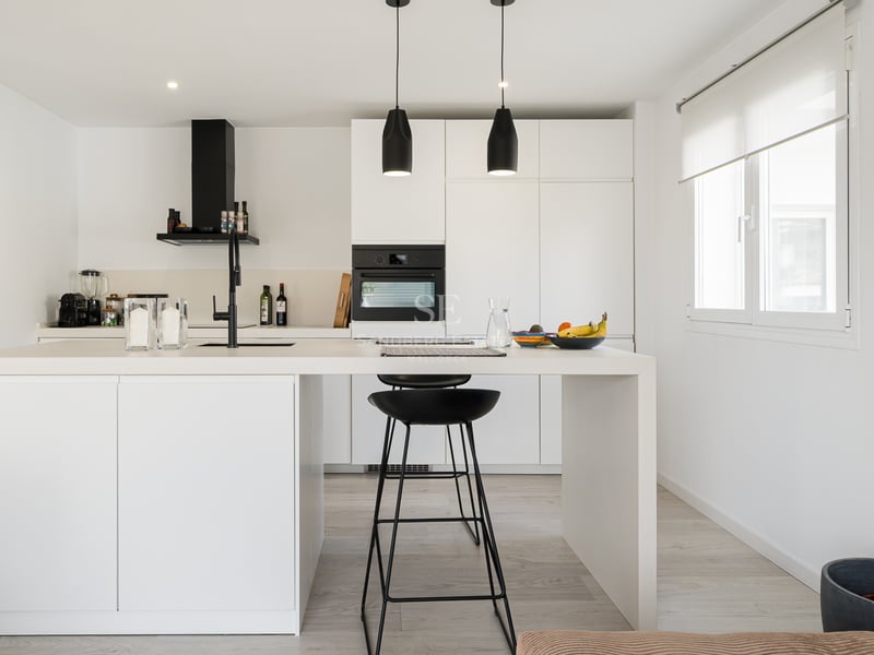 Cuisine blanche lumineuse dotée d'un grand îlot central avec des tabourets noirs et des suspensions noires.