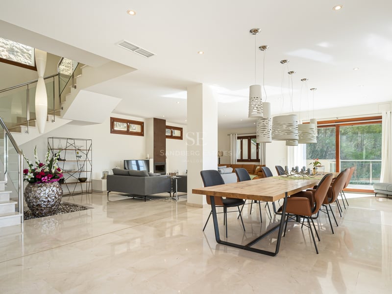 Salle à manger moderne à plan ouvert avec sol en marbre, grande table en bois, luminaires design et escalier en pierre.