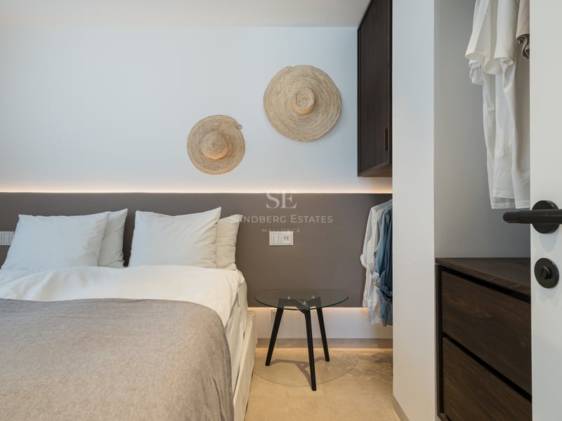 Chambre moderne avec tête de lit rétroéclairée, draps blancs et chapeaux de paille décoratifs au mur.