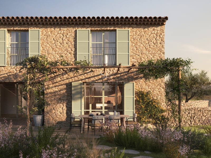 Façade en pierre avec volets vert sauge et pergola rustique surplombant un coin repas extérieur dans un jardin.