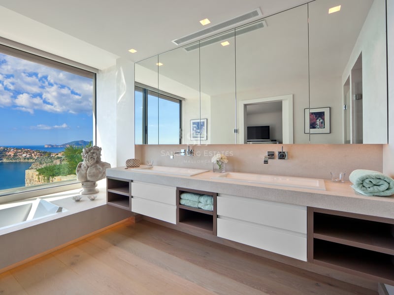 Salle de bain moderne avec double vasque et grande baie vitrée offrant une vue panoramique sur la mer.
