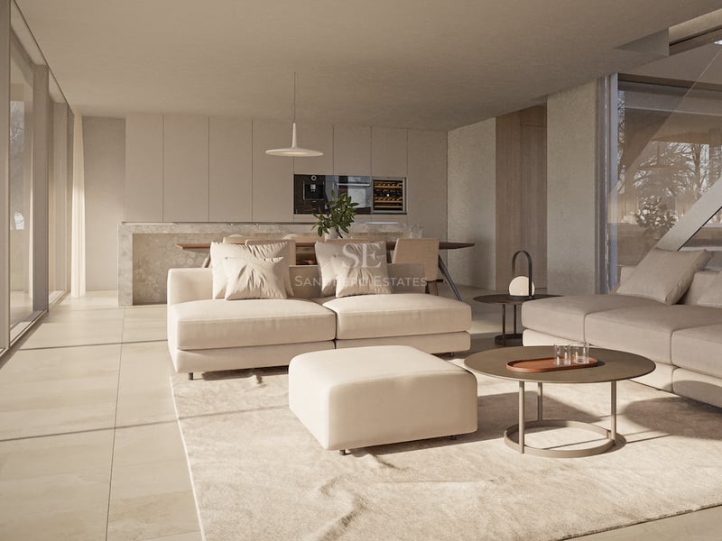 Salon moderne avec canapé crème, pouf et table basse ronde s'ouvrant sur une salle à manger épurée.