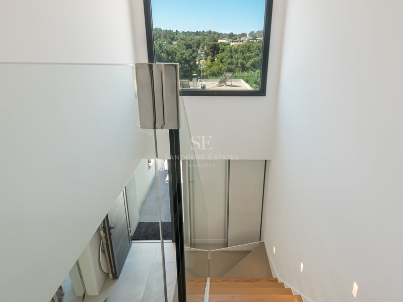 Vue intérieure d'un escalier en chêne avec garde-corps en verre donnant sur un paysage méditerranéen verdoyant.