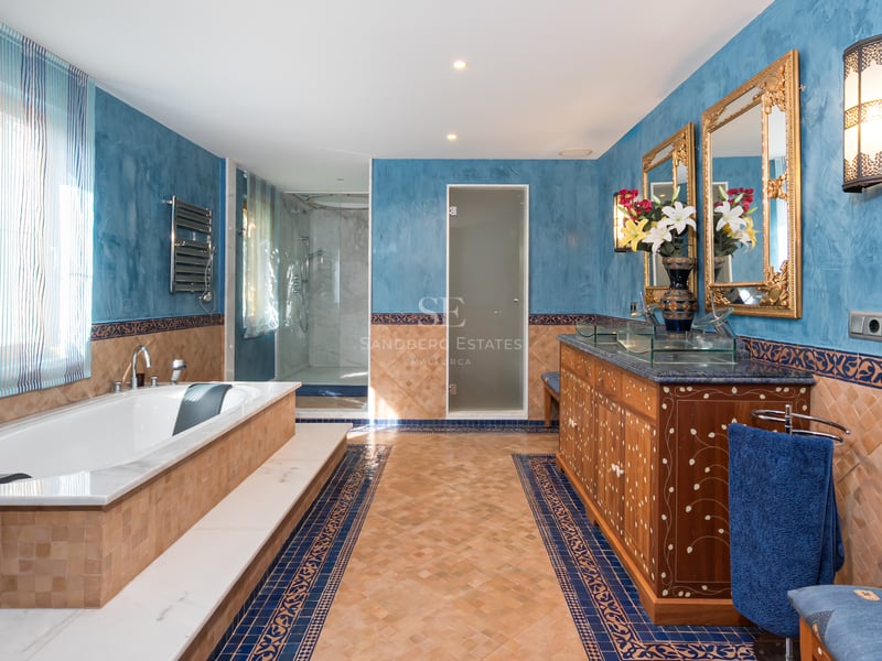 Salle de bain de prestige avec baignoire intégrée, meuble en bois travaillé, miroirs dorés et murs bleus texturés.