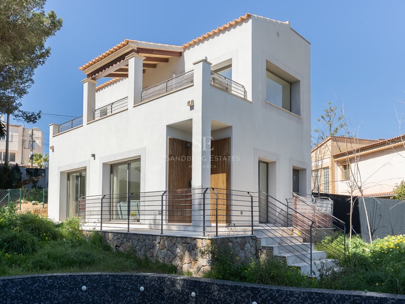 Villa moderne blanche de deux étages avec base en pierre naturelle et toit en terre cuite sous un ciel dégagé.