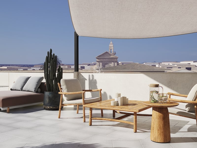Terraza moderna con muebles de teca, vela de sombra y vistas a un campanario histórico bajo un cielo despejado.
