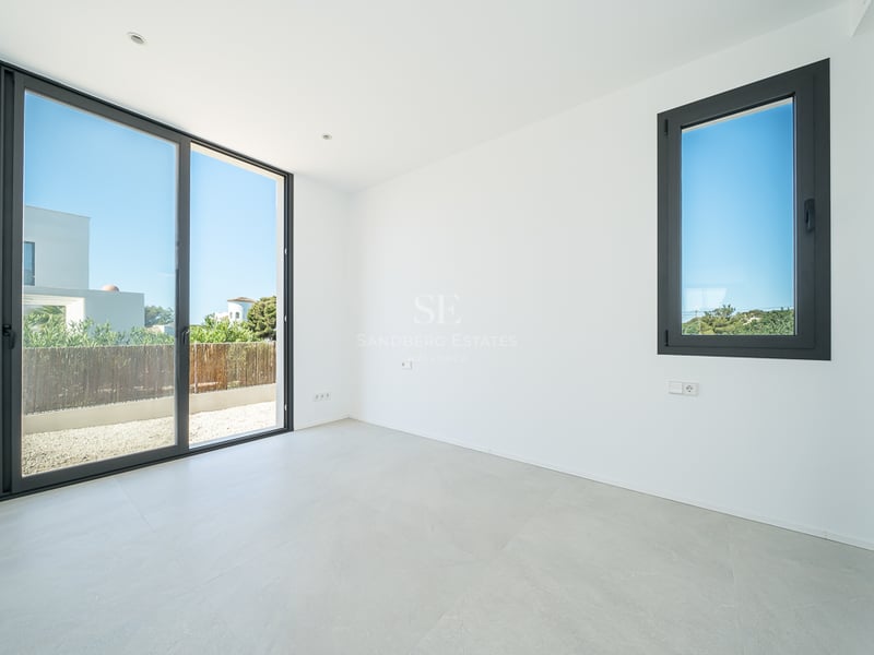Pièce moderne vide avec murs blancs, sol en carrelage gris et une grande porte vitrée coulissante.