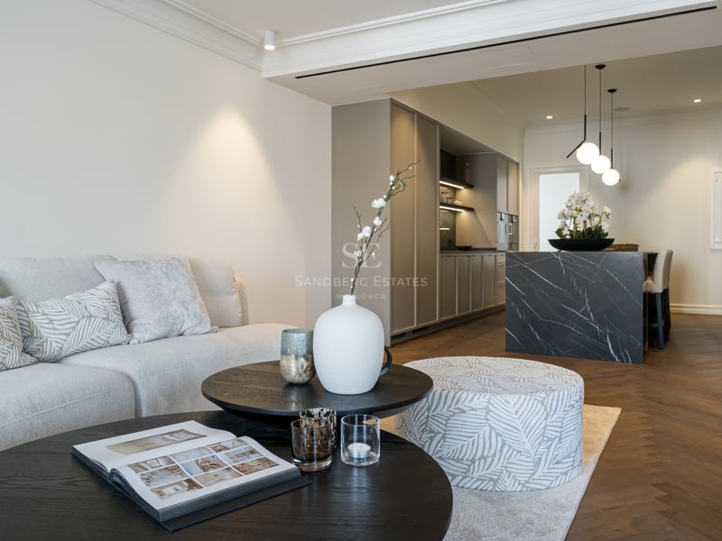 A contemporary open-plan living room and kitchen featuring herringbone floors, a dark marble island, and neutral furnishings.