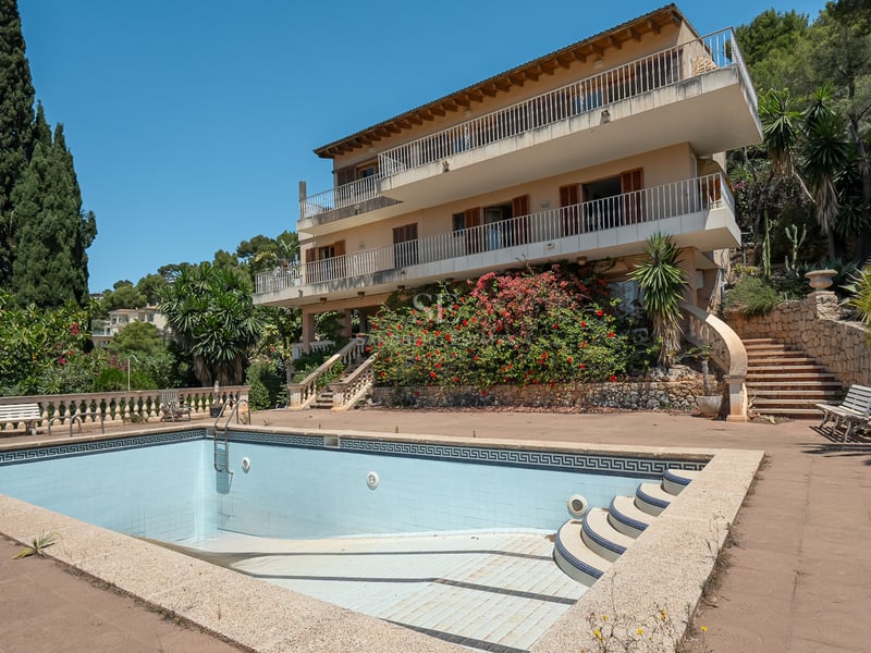 Grande piscine privée devant une villa méditerranéenne de trois étages avec terrasses et jardins luxuriants.