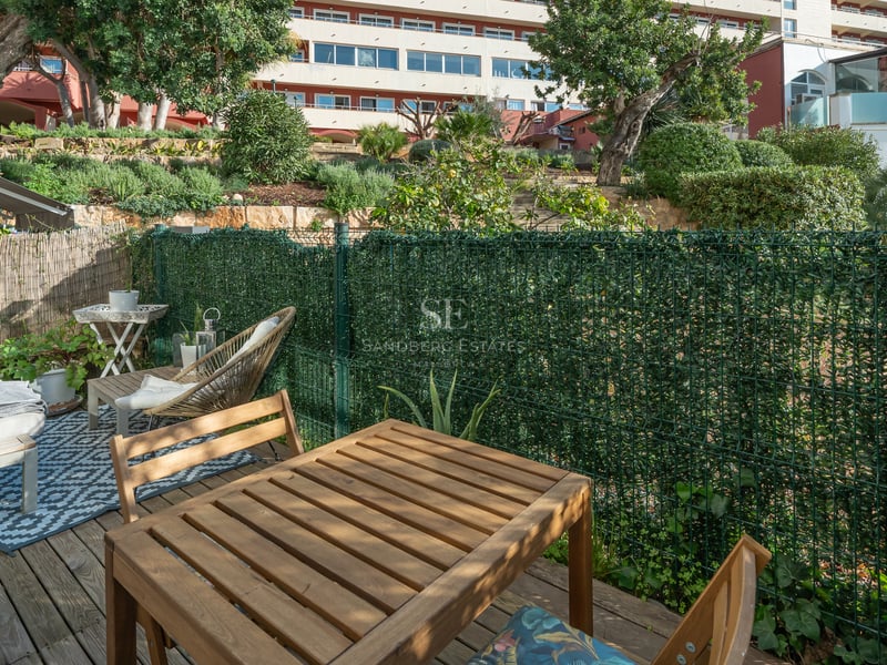 Terrasse ensoleillée avec table à manger en bois, coin détente et clôture de confidentialité verdoyante.