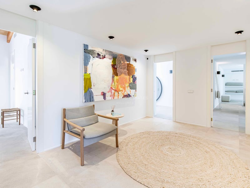 Couloir minimaliste avec sol en pierre naturelle, tapis rond en jute, fauteuil en bois et peinture abstraite.