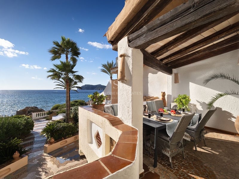 Terrasse couverte avec poutres en bois, table à manger, chaises en osier et vue imprenable sur la mer et les palmiers.