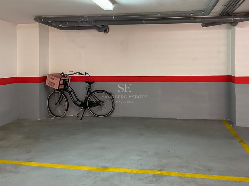 Place de parking numérotée avec murs gris et blancs, bande rouge et sol en béton avec lignes jaunes.