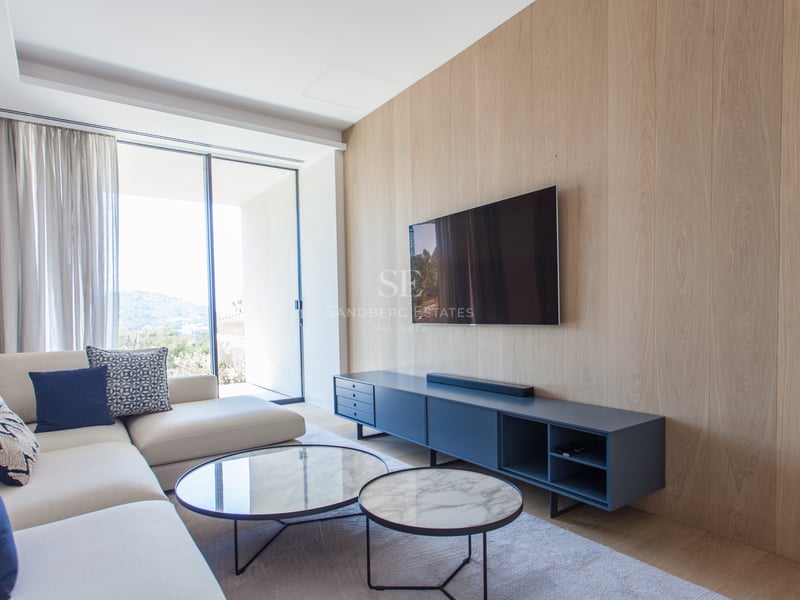 Salon moderne avec mur en chêne, télévision murale, tables en marbre et grandes baies vitrées vers les collines.