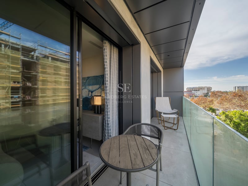Balcon contemporain avec garde-corps en verre, table en bois et sièges donnant sur un parc.