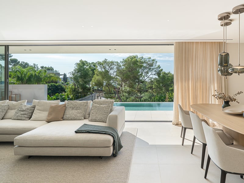 Salon moderne élégant avec canapé beige, coin repas et grandes baies vitrées ouvrant sur une terrasse avec piscine.