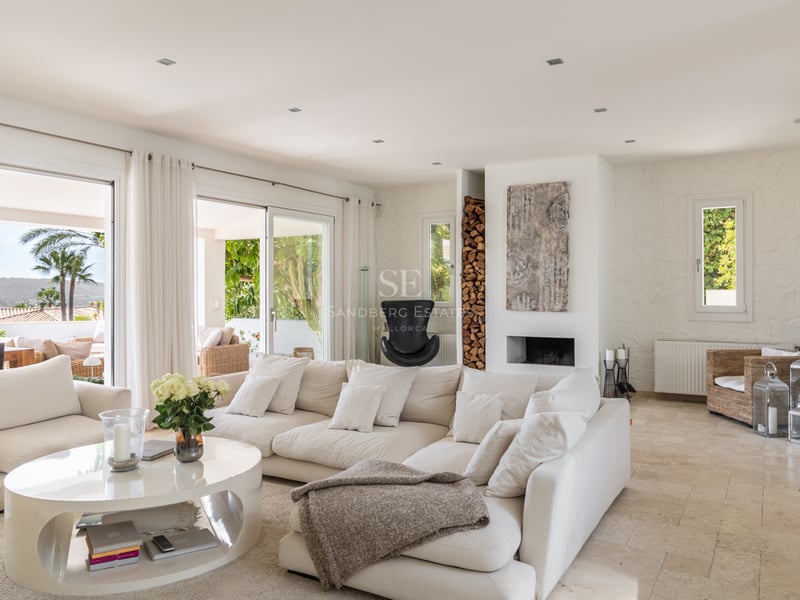Grand salon aux tons crème avec sol en travertin et baies vitrées ouvrant sur une terrasse ensoleillée.