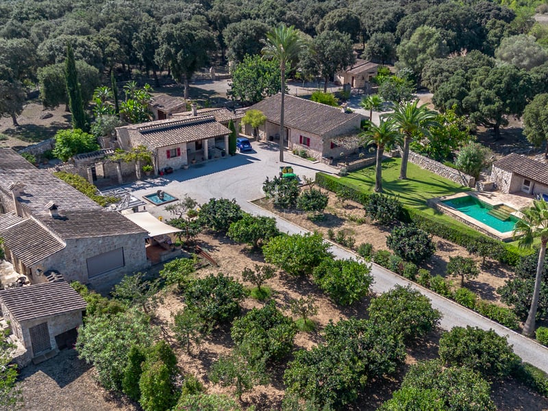 Vue aérienne d'un domaine en pierre avec plusieurs bâtiments, une piscine et de vastes vergers à Majorque.
