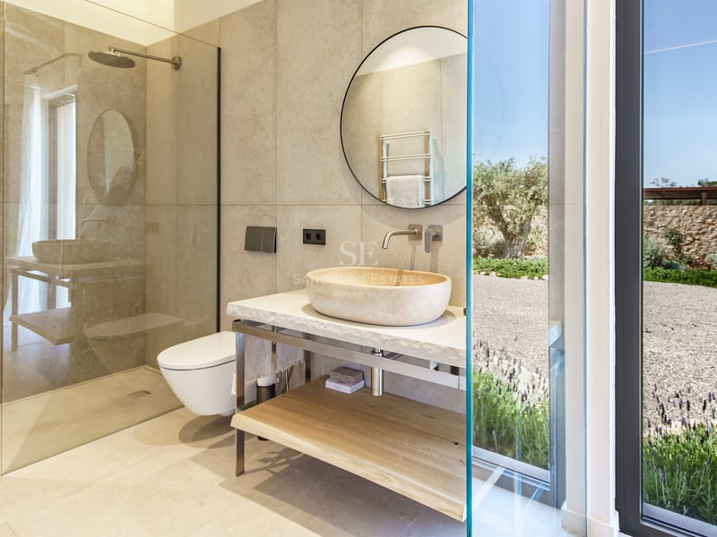 Baño contemporáneo con lavabo de piedra natural sobre encimera, espejo circular y ducha a ras de suelo.