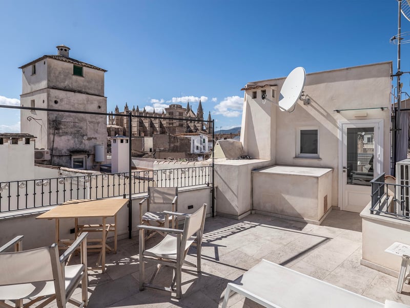 Toit-terrasse spacieux avec mobilier en bois et vue imprenable sur la cathédrale historique sous un ciel bleu.