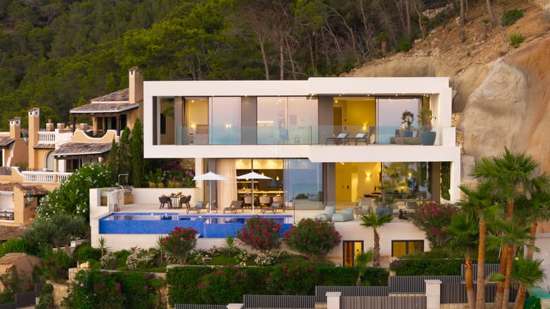 Fassade einer modernen zweistöckigen weißen Villa mit Infinity-Pool und großen Glasfronten in der Dämmerung.