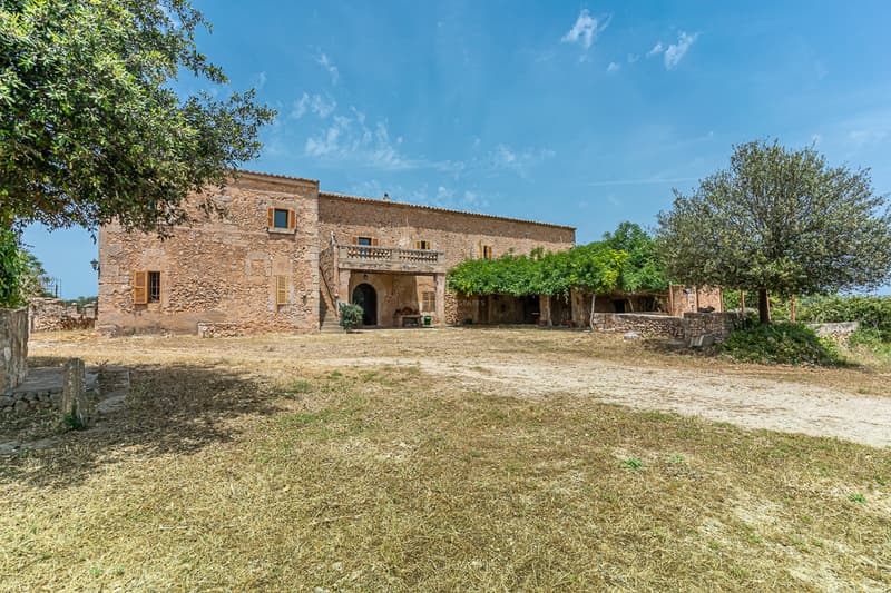 Large two-story rustic stone villa with wooden shutters and a balcony under a clear blue sky.