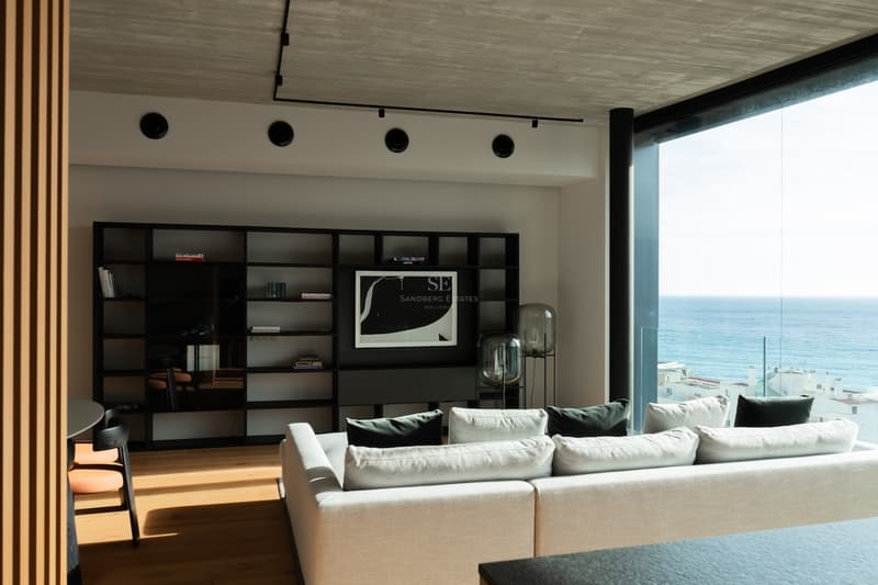Zeitgenössisches Wohnzimmer mit bodentiefen Fenstern zum Meer, Eichenparkett und einem eleganten schwarzen Regal.