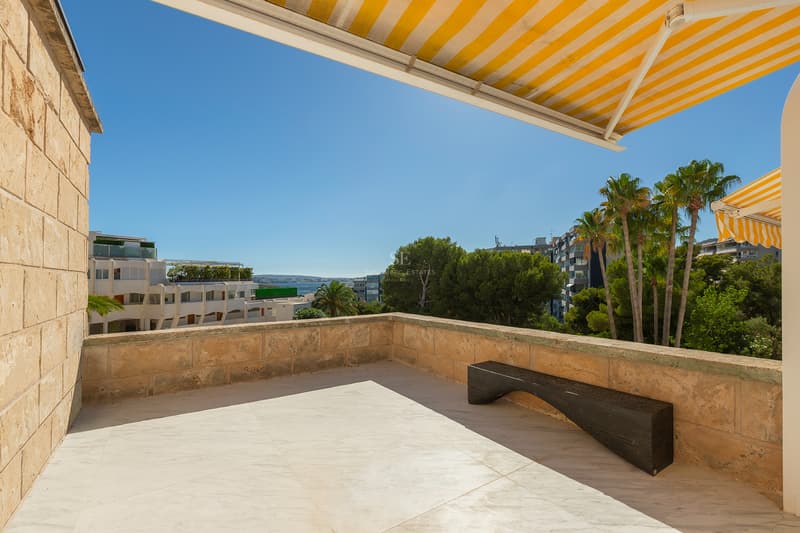 Spacious marble terrace featuring natural stone walls, a minimalist wooden bench, and yellow striped awnings.