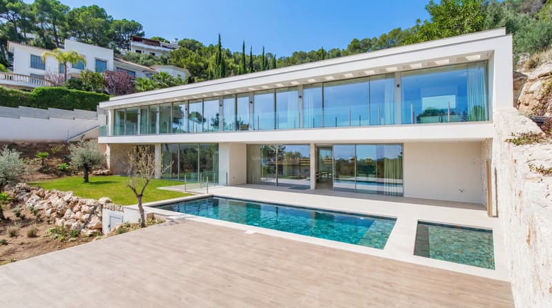Tvåvånings modern vit villa med stora glasfönster framför en rektangulär pool och träterrass.