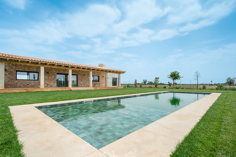 Gran piscina rectangular con azulejos turquesa junto a una villa tradicional de piedra y césped impecable.