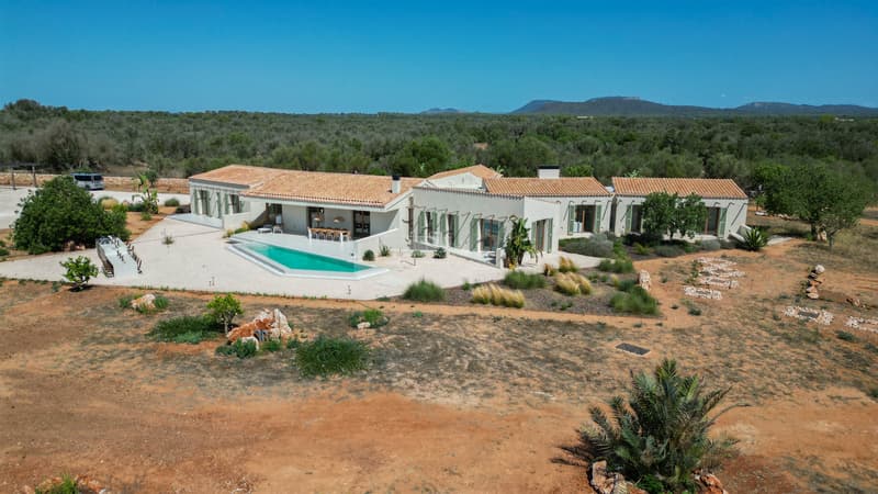 Vista aérea de una villa moderna de una planta con techos de terracota, piscina geométrica y entorno natural extenso.