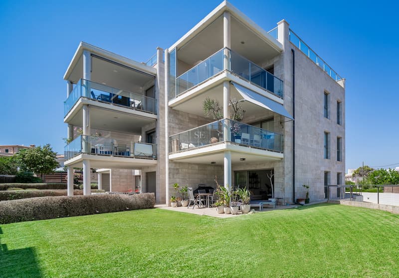 Trevånings modern villa med naturstensfasad, glasbalkonger och grönskande gräsmatta under en klarblå himmel.